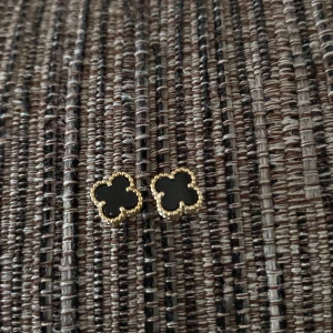 Svarta klöverformade örhängen i guld - Snygga örhängen i klöverform med svart mitt och guldfärgad kant. Perfekta för dig som gillar stilrena accessoarer med en twist. De är små och diskreta men ändå riktigt trendiga, passar till alla dina outfits.