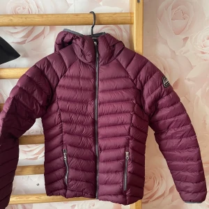 Vinröd pufferjacka från McKinley - Säljer en vinröd pufferjacka från McKinley i storlek 34. Jackan har huva, två dragkedjeförsedda fickor och quiltad design. Perfekt för kyliga dagar och har en snygg, sportig look med McKinley-logga på ärmen.
