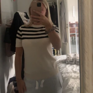 Randig topp från MNG i vitt och svart - Säljer en snygg kortärmad topp från MNG med breda svarta och vita ränder upptill och enfärgat vitt nedtill. T-shirten har rund halsringning och är i ett mjukt, stretchigt material. Perfekt för en chill och stilren look.