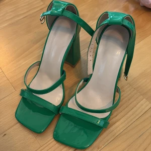 Gröna sandaler med klack och remmar - Helt oanvända. Storlek 37. Trendiga gröna sandaler med bred klack och smala remmar över foten och runt vristen. Skorna har fyrkantig tå och glansig finish som ger en modern vibe. Perfekta för att lyfta din outfit med en färgklick.