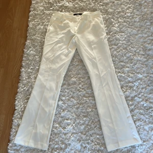 Vita bootcut kostymbyxor från Bikbok - Snygga vita kostymbyxor från Bikbok i storlek 38. De är lågmidjade och byxorna har bootcut-ben och klassisk midja, med fickor fram och bak. Perfekt för dig som gillar stilrena och fräscha looks. Materialet känns mjukt. Aldrig andvända. 