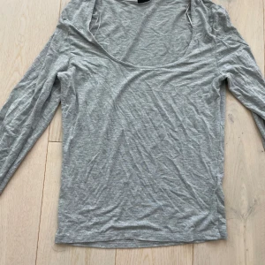 Grå långärmad topp med rund hals - Snygg grå långärmad topp i mjuk bomull med rundad, djup halsringning. Perfekt för lager-på-lager och enkel att matcha med jeans eller kjol.