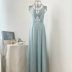 Vintage Olga långklänning med spetsdetaljer (tag cut) - Säljer en drömmig blå långklänning med djup v-ringning och spetsdetaljer. Ganska lång (kan täcka hela fötter om du är kortare än 160cm). Några håll täcks av fina brodderade blommor. Verklig färg i 4:e bild. Storlek: M (36-38). Dockans storlek: 34.