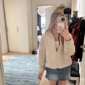 Beige teddyjacka från H&M - Supermysig beige teddyjacka från H&M med dragkedja framtill och två fickor. Jackan är croppad och har en avslappnad passform med långärmade ärmar. Perfekt för kyliga dagar när du vill vara både varm och snygg.