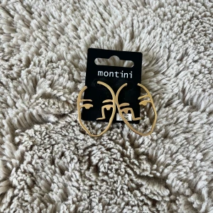 Guldiga ansiktsörhängen från Montini - Unika örhängen från Montini i guldigt metall med coolt ansiktsmotiv. Perfekt statement-accessoar för dig som vill sticka ut och addera lite edge till din look. Säljs i par och har en modern, konstnärlig design. Helt oanvända med prislapp