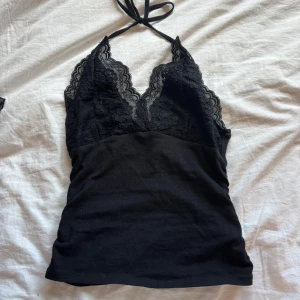 Svart linne med spets överdel. - Supersnygg svart linnetopp med halterneck och djup v-ringning. Överdelen är dekorerad med blommig spets och har tunna knytband i nacken. Toppen är figurnära och passar perfekt till jeans eller kjol för en trendig look.