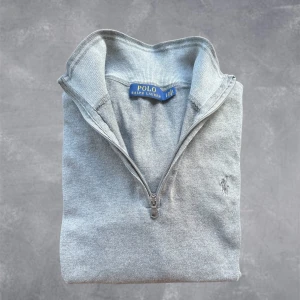 Grå half zip tröja Polo Ralph Lauren - Snygg grå långärmad tröja från Polo Ralph Lauren med half zip och klassisk krage. Tröjan har broderad logga på bröstet och är tillverkad i mjuk bomull. Perfekt för lager-på-lager och chill stil.