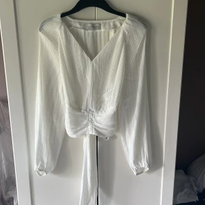 Vit blus från Anna Field - Supersnygg vit blus från Anna Field med plisserat tyg, v-ringning och långa ärmar. Den har knyt i midjan och lätt glansigt material som ger en lyxig känsla. Har använt fåtal gånger💓
