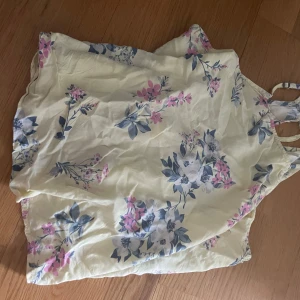 Blommig linnetopp från Hollister - Supersöt linnetopp från Hollister i ljusgul nyans med blommigt mönster i blått och rosa. Tunt och luftigt material, perfekta smala axelband och avslappnad passform. Perfekt för varma dagar och somriga vibes!
