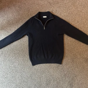 Mörkblå Kashmir tröja ifrån Soft Goat - Snygg mörkblå Kashmir tröja från Soft Goat med half zip-dragkedja i halsen. Tröjan har lång ärm, ribbade muddar och klassisk passform. Perfekt för lager-på-lager och funkar året runt när du vill vara både chill och stilren. Det finns tyvärr ett litet hål på armbågen annars är den i mycket bra skick 