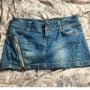 lågmidjade Jeanskjol - Snygg blå jeanskjol från Fishbone med cool sned dragkedja framtill och klassiska fickor både fram och bak. Knappt använd köpte second hand utomlands. Dragkedjan är lite svår att dra upp och ner ibland men inget som påverkar hur kjolen ser ut på 