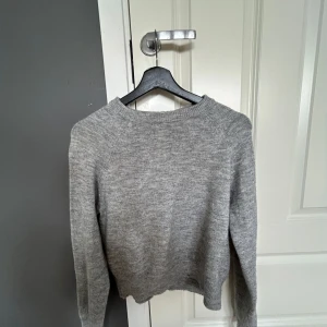 Grå stickad tröja från H&M Divided - Enkel och stilren grå stickad tröja från H&M Divided. Tröjan har rund halsringning, långa ärmar och ribbade muddar. Perfekt att slänga på sig när det är kyligt ute. Passar dig som gillar en clean och avslappnad look.