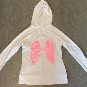 Vit hoodie med rosa vingar Victoria's Secret - Jättefin vit hoodie från Victoria's Secret med dragkedja. På ryggen finns stora glittriga rosa vingar och dragkedjan liknar små silverfärgade vingar. Säljer då jag inte tyckte att den passade mig så som jag ville🥰Köpte här på Plick för ett tag sedan men jag själv har aldrig använt den💕