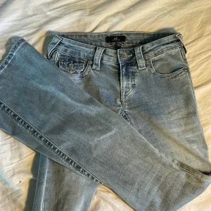 True Religion Joey Low Rise Flare Jeans - Snygga ljusblå jeans från True Religion, modell Joey Low Rise Flare. De har låg midja, utsvängda ben och klassiska detaljer som markerade sömmar och fickor med lock och knappar bak. Perfekta för dig som gillar retrovibbar och cool streetstil. Använd typ 1 gång