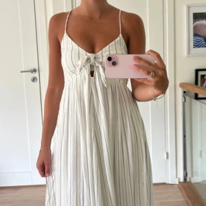 Vit långklänning med smala ränder - Superfin vit långklänning med tunna reglerbara axelband och knyt framtill. 