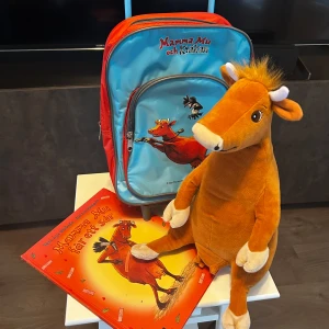 Mamma Mu, en bok och liten dragväska /ryggsäck - Säljer ett  litet paket med mamma mu och kråkan motiv. Innehållande en liten resväska med hjul. Kan också bäras som ryggsäck. Själva mamma mu (30 cm) och en bok om mamma mu givetvist. 