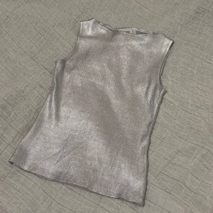 Silver Weekday -  Silverfärgad topp från Weekday i storlek S. Toppen är ärmlös med boatneck och har en snygg, metallisk finish som verkligen sticker ut. Perfekt för dig som vill ha något extra till outfiten. Helt oanvänd