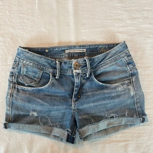Blå jeansshorts från Fornarina - Snygga långmidjade blå jeansshorts från Fornarina med slitna detaljer och uppvikta benslut, som går att vika ner. Perfekta för sommaren!! Köpte på loppis för 400kr så vet inte hur använda de är men mycket fint skick iaf. Aldrig använda av mig, var för små. Kom med prisförslag!!