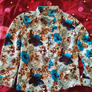 Blommig skjorta med färgglada detaljer - Så fint blommig skjorta i retrokvalité som jag älskat men inte får användning för längre. Perfekt i sommar! Köpt secondhand men i helt felfritt skick förutom att guldet flagnat lite från några knappar, vilket knappt märks. Lite större oversized M.  