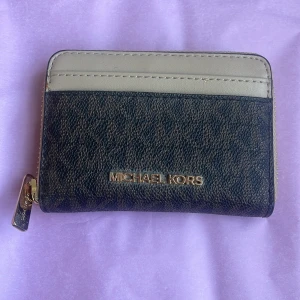 Michael Kors plånbok i beige och mörkbrun - Snygg plånbok från Michael Kors i beige och mörkbrunt skinn med guldfärgad dragkedja. Plånboken har flera kortfack och ett rymligt myntfack. Perfekt storlek för att få plats i mindre väskor och enkel att ta med överallt. Nypris ca 1100kr, aldrig använt.