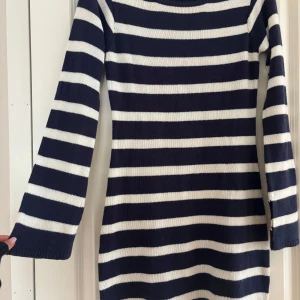 Randig stickad klänning från Nelly - Mysig stickad klänning från Nelly i marinblått och vitt med breda horisontella ränder. Modellen är kort och har långa ärmar. Perfekt för dig som gillar en klassisk och chill stil. Materialet är mjukt och stretchigt, vilket gör den superbekväm. 