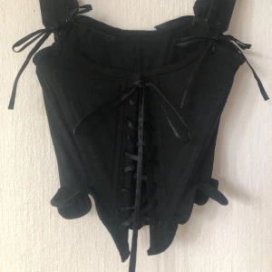 Svart korsett topp🌷 - Säljer en svart korsett med breda axelband och snygg snörning framtill. Modellen har en cool, markerad midja och dekorativa knytband på axlarna. Svart denim✨ Handsydd av mig✨ Kan bäras med eller utan axelbanden beroende på vad man tycker är snyggast!✨ Väldigt bekväm att ha på sig✨ Sydd efter ett mönster från 1790 så den ger en markerad midja✨