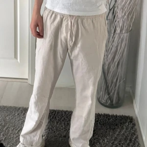 Beiga linnebyxor  - Snygga och luftiga beiga linnebyxor med resår och snörning i midjan. Byxorna har raka ben och en avslappnad passform, perfekta för varma dagar. Materialet är linne vilket gör dem svala och bekväma att bära.