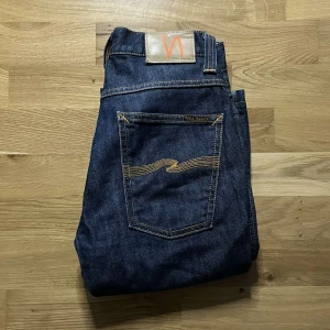 Nudie Jeans Slim Jim - Snygga mörkblå jeans från Nudie Jeans, modell Slim Jim Dry Brown. Klassisk femficksdesign med raka ben och kontrastsömmar på bakfickorna. Tillverkade i 100% bomull för en autentisk jeanskänsla. Perfekta för dig som gillar stilrena och tidlösa jeans. Uppsydda till L30 ! Längd ca 100cm