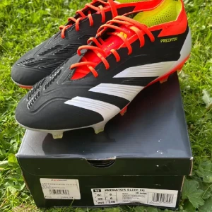 Adidas Predator Elite FG fotbollsskor - Säljer ett par Adidas Predator Elite FG fotbollsskor i svart, vitt och neonrött med gula detaljer. Skorna har snörning, mönstrad ovandel och plös samt dobbar för fast mark. Perfekta för dig som vill sticka ut på planen med grym känsla och stil. Helt nya prislappen finns kvar. Aldrig används, säljs pågrund av för småa. 
