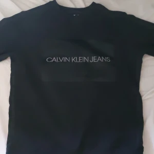 Svart sweatshirt Calvin Klein Jeans XS - Svart sweatshirt från Calvin Klein Jeans i storlek XS. Tröjan har rund halsringning, långa ärmar och en clean look med logga tryckt framtill. Tillverkad i mjuk bomullsblandning som är skön att ha på sig. Perfekt för en stilren och avslappnad vibe.