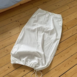 Cargo skirt balongkjol med dragsko - Vit långkjol / cargo skirt / balongkjol i bomull med snörning i midjan och nertill. Kjolen har stora fickor på sidorna och en slits på ena sidan. Lätt genomskinlig! Storlek L men passar också S-M tack vare dragsko i midjan. Bästa sommarkjolen som tyvärr inte används.