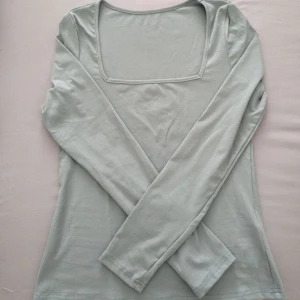 Ljusgrön långärmad topp med fyrkantig ringning - En stilren ljusgrön långärmad topp med snygg fyrkantig ringning. Tunn och mjuk i materialet, perfekt att matcha med jeans eller kjol. Enkel design som känns fräsch och modern.