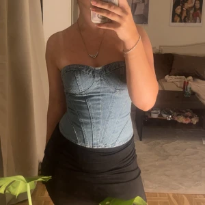 Ljusblå jeanskorsett med markerade sömmar - Säljer en snygg ljusblå korsett i jeanstyg med markerade sömmar och formade kupor. Toppen är axelbandslös och har en tight passform som framhäver midjan. Perfekt att styla med kjol eller jeans för en cool look.