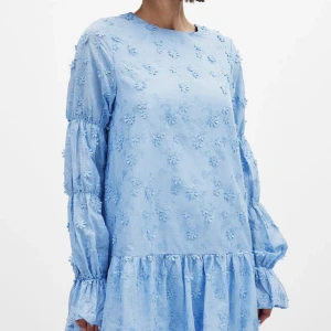 NAKD Blå blommig klänning med öppen rygg - Eftertraktad NAKD Supersöt ljusblå klänning med broderade blommor, volangkant och långa puffärmar. Klänningen har öppen rygg med knytband och en luftig, flowy passform. Jätte bra skick 