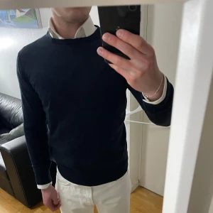 Mörkblå ulltröja från Zara Man - Snygg mörkblå rundhalsad tröja från Zara Man i 100% extrafin ull. Klassisk modell med lång ärm och ribbade muddar. Perfekt att bära över en skjorta för en clean och stilren look. Sitter som S
