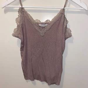 Beige ribbad linnetopp från Amisu - Supersöt beige ribbad linnetopp från Amisu med tunna axelband och spetsdetaljer längs v-ringningen och axlarna. Toppen har en mjuk, stretchig känsla och är perfekt för lager-på-lager eller till jeans. Spetsen ger en romantisk vibe och den ribbade strukturen gör den extra snygg.