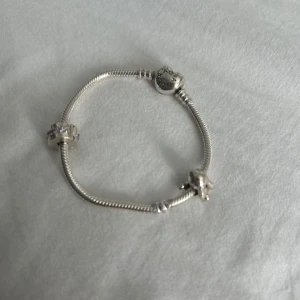 Pandora silverarmband med berlocker - Superfint Pandora armband i silver med hjärtformad låsdetalj. Armbandet har två berlocker: en söt kanin i silver och en rund berlock med rosa stenar. Priset är diskuterbart och kom privat vid frågor och funderingar🤗