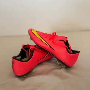 Nike Mercurial vapor 10 fotbollsskor  - Säljer ett par Nike Mercurial fotbollsskor i neonrött med svarta och gula detaljer. Fick från Nike lager kontakt. Sulan har dobbar för bra grepp på planen och en svart Nike-logga undertill. Perfekta för dig som vill sticka ut. Passar även 43