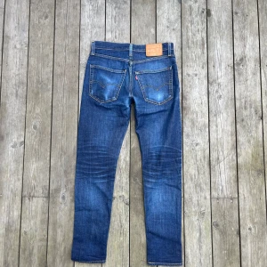 Levi's 512 blå jeans W30 L32 - Snygga Levi's 512 jeans i klassisk blå denim med lätt slitning och smal passform. Jeansen har fem fickor, gylf med dragkedja och ikonisk läderpatch bak i midjan. Perfekta för dig som gillar en modern och stilren look.