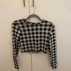 Rutig minikjol med fickor med en tröja till - Supersnygg kortkjol i grått och svart rutigt mönster. Kjolen har två stora fickor framtill med lock och är figursydd för en tight passform. Till kjolen finns en matchande topp till. Den är en magtröja eller croptop som det brukar heta.