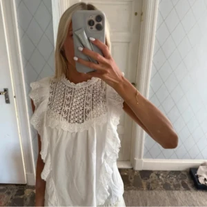 Vit blus med spets och volang - Supersöt vit blus med broderad spets upptill och volangdetaljer längs axlarna. Ärmlös modell med romantisk känsla och rund halsringning. Perfekt för dig som gillar en feminin och trendig look. Tillverkad i mjukt bomullstyg. Köpte härifrån och säljer nu vidare då den ej kommer till användning. Lånade bilder ställ gärna frågor om ni har kan även ta egna bilder om så önskas🌺