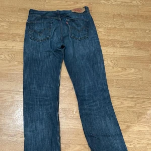 Levi's 501 mörkblå jeans straight fit - Klassiska Levi's 501 jeans i mörkblå tvätt med raka ben och knappgylf. Jeansen har fem fickor, tydliga sömmar och den ikoniska läderpatchen bak i midjan. Perfekta för dig som gillar en tidlös och avslappnad look.