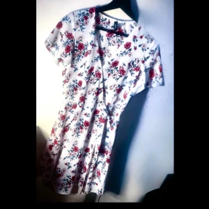 H&M - Omlottklänning - Helt ny/oanvänd! Vit, blommig omlottklänning med rosettknytning, väldigt enkel att ta av & på genom att knyta upp rosetten då det finns en knapp i urringningen samt en på höger sida av midjan, storlek 36 (S). Den är verkligen en perfekt sommarklänning för de varmaste dagarna/kvällarna då den har ett väldigt tunt & luftigt tyg men ändå inte genomskinlig alls. Erbjuder rabatt vid köp av 2 eller fler produkter!