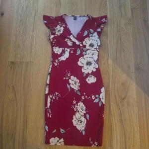Röd blommig klänning  - Superfin röd kortklänning från SHEIN med stora vita och beige blommor.Klänningen har v-ringning, volangärmar och figurnära passform. Perfekt för dig som vill sticka ut med ett färgstarkt mönster och snygg siluett. Sitter jättebra på kroppen och fångar upp allas uppmärksamhet. Passat bra på en night out med vänner 😉 eller kanske till och med en dejt...😏 när man väl har på sig den så kommer man älska den kära vänner. Aldrig använd! Fick den som present från någon jag hatar så måste bli av med den!