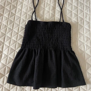 Svart smockad linnetopp Gina Tricot - Supersöt svart linnetopp från Gina Tricot med smockad överdel och tunna axelband. Toppen har en lätt utställd nederdel och är perfekt för varma dagar. Har bara använt ca3 ggr då den är för stor. Pris går att diskutera🥰