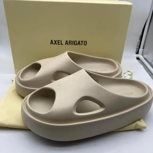 Beige sandaler Axel Arigato - HELT NYA MED BOX/KVITTO. Chunky beige sandaler från Axel Arigato med modern, minimalistisk design. De har öppen tå, platt sula och coola utskurna detaljer på sidorna. Tillverkade i syntetmaterial och perfekta för en avslappnad och trendig look.