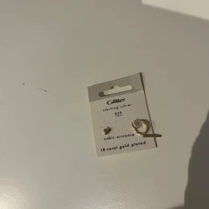 Guldpläterade örhängen från Glitter - Säljer ett par snygga örhängen från Glitter i  guldpläterat sterling silver. Ena örhänget är ett litet örhängen med tre sirklar plupp med cubic zirconia-stenar, det andra är ett litet örhänge med hängande detalj. Perfekt för dig som gillar mixade stilar!