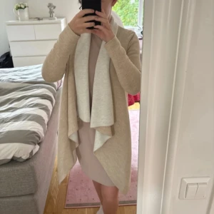 Beige cardigan jacka med vattenfallsfront - Säljer en supermjuk och lång cardigan jacka i beige med ljusare insida. Jackan har en snygg vattenfallsfront och är långärmad, perfekt att slänga på sig över en outfit för en chill och stilren look.