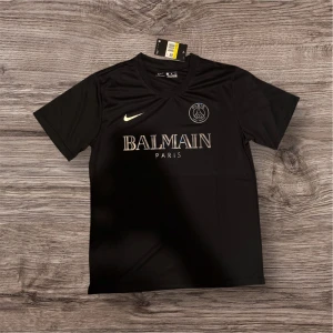 Svart PSG x Balmain fotbollströja Nike - Snygg svart fotbollströja från Nike i samarbete med PSG och Balmain. Tröjan har korta ärmar, rund hals och tryck med Balmain Paris-logga samt PSG-emblem på bröstet. Tillverkad i ett lätt och sportigt material som andas.
