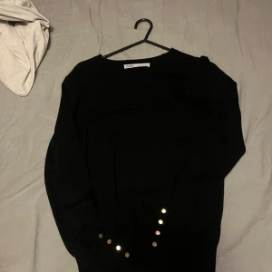 Svart tröja från Zara - Svart tröja från Zara med rund halsringning och dekorativa guldfärgade knappar vid ärmslutet. Perfekt för dig som gillar en enkel men ändå snygg look. Långärmad och mjuk i materialet.